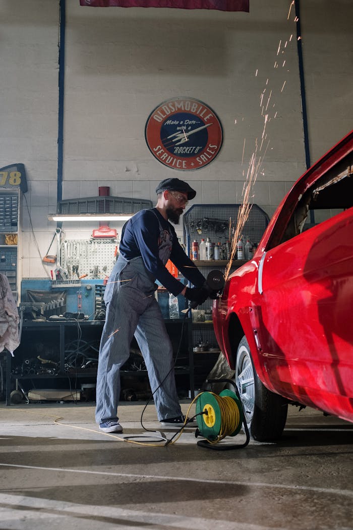 Mechanic using grinder on car body in a busy garage, sparks flying as he works.