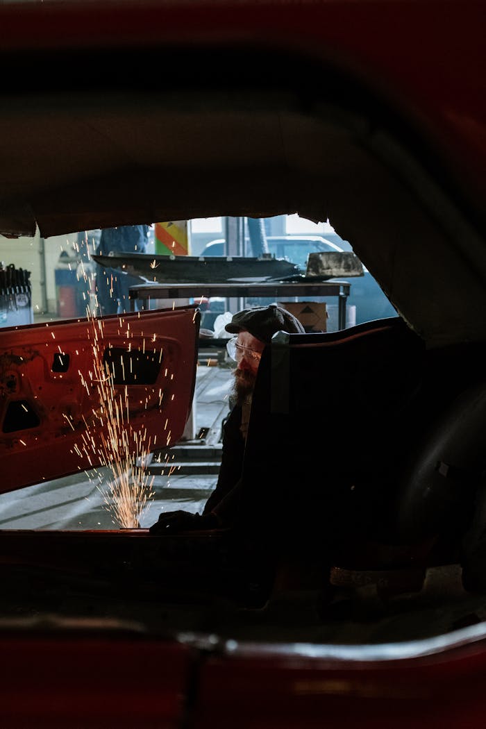 About A mechanic performs welding inside a car at a workshop, showcasing sparks and repair work.