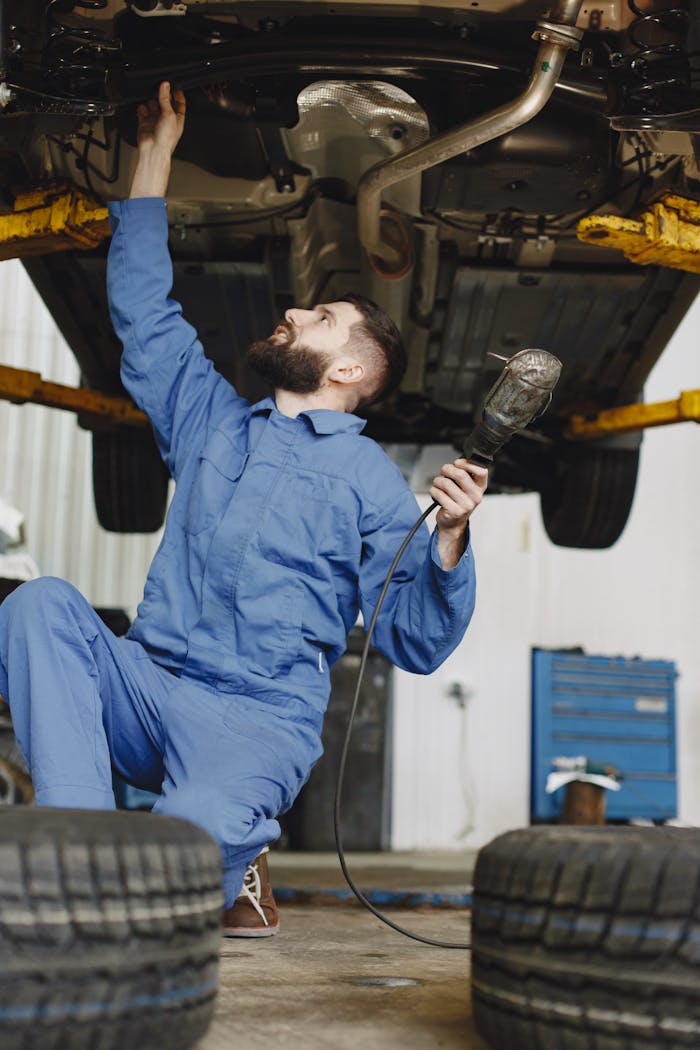 Mechanic in workwear inspecting vehicle underside in a garage environment. Service and maintenance concept.